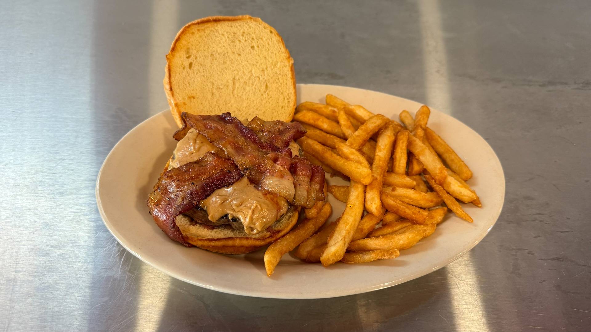 A Goober Burger from Brooks Burgers, featuring a juicy beef patty topped with melted cheese and a spread of creamy peanut butter, served on a toasted bun with a side of crispy French fries.