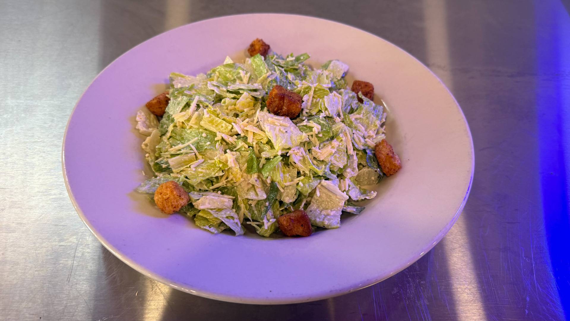 A beautifully plated Caesar salad with fresh romaine lettuce, grated Parmesan cheese, croutons, and Caesar dressing served on a rustic wooden table at Brooks Burgers in Naples, Florida