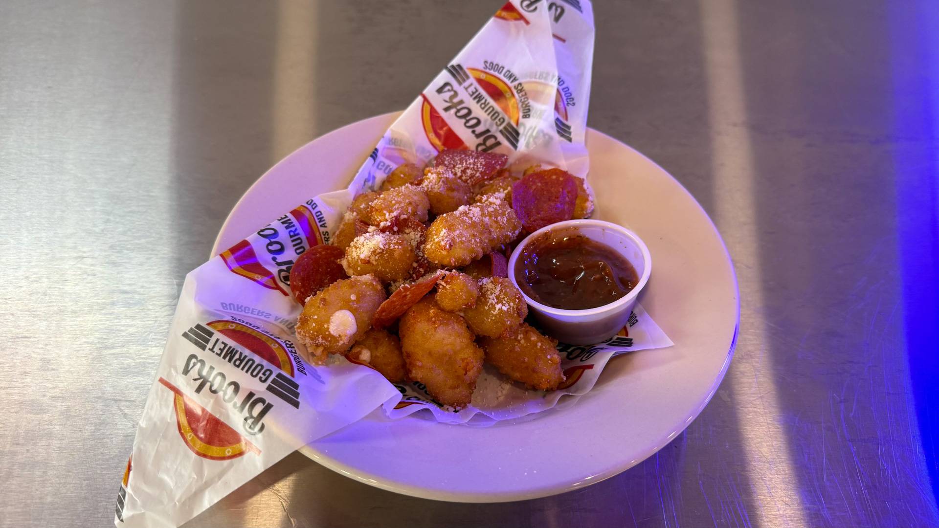 A plate of golden crispy Wisconsin cheese curds accompanied by a dipping sauce, served at Brooks Burgers in Naples, showcasing a delicious appetizer experience